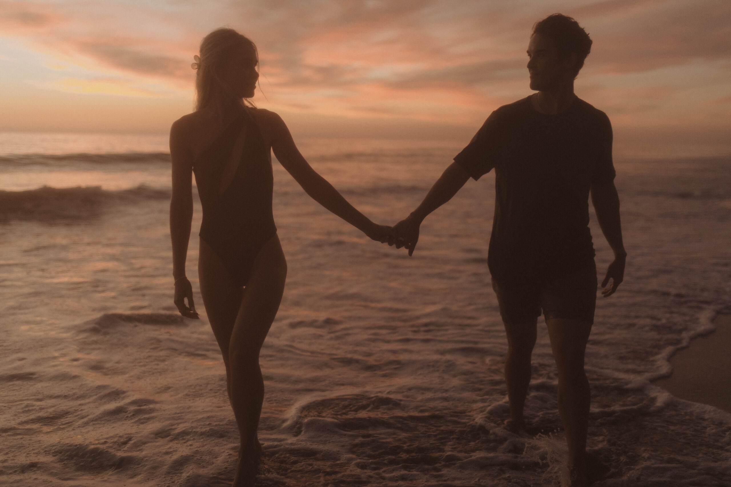 Man and woman holding hands in the ocean during sunset