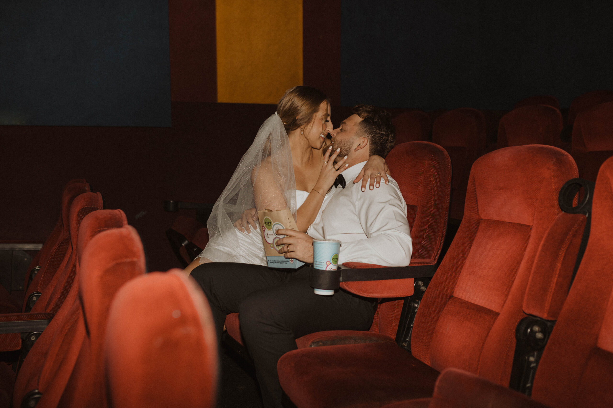 Elopement couple sitting in a movie theater feeding each other popcorn