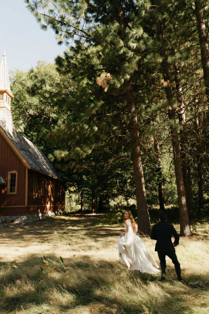 Newlyweds walking through the trees near Yosemite Valley Chapel during their intimate wedding