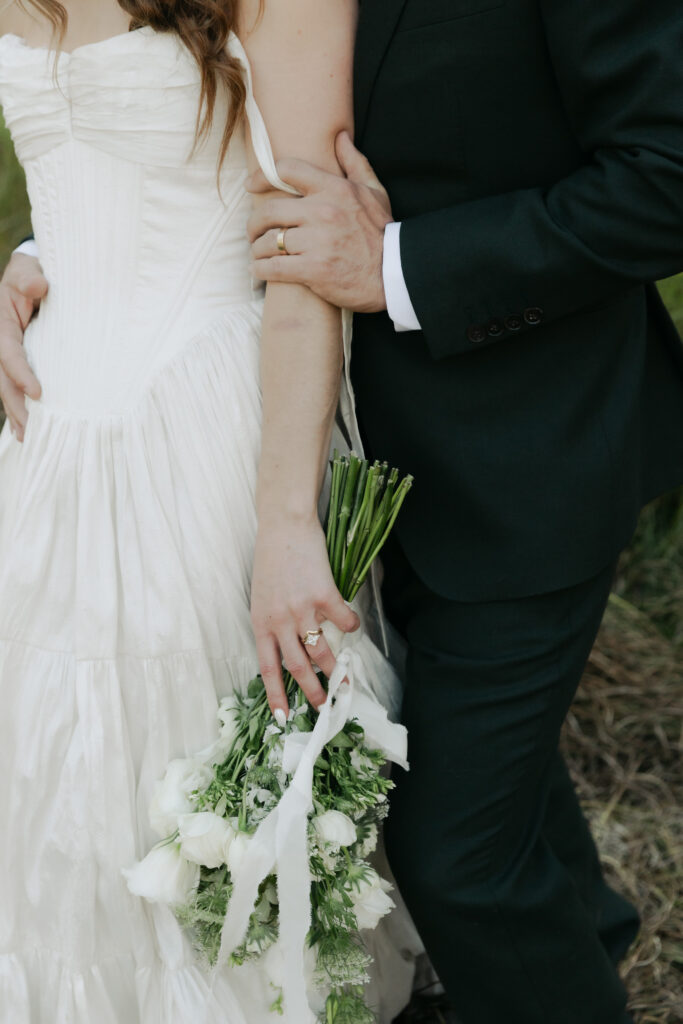 Detail of newlyweds holding each other with the bride’s bouquet during their Yosemite wedding