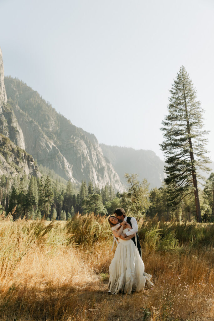 Bride and groom embracing in a golden meadow surrounded by Yosemite Valley mountains