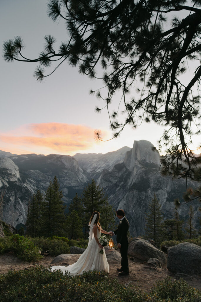 Couple overlooking Half Dome beneath pink sunrise clouds during their Glacier Point elopement