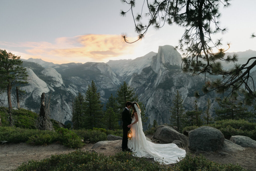 Bride and groom standing beneath pink sunrise clouds with Half Dome at Glacier Point