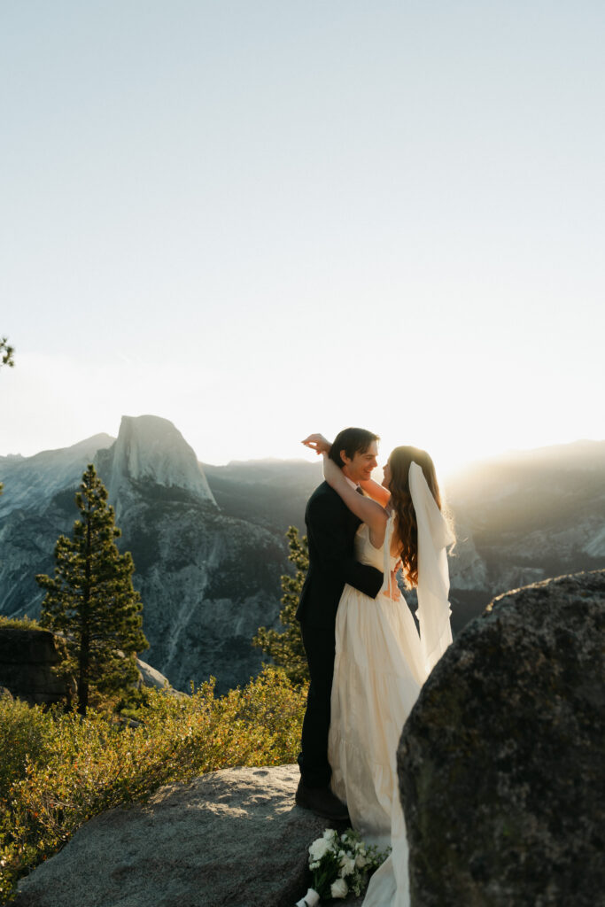 Bride and groom embracing at sunrise with Half Dome behind them during their Glacier Point elopement